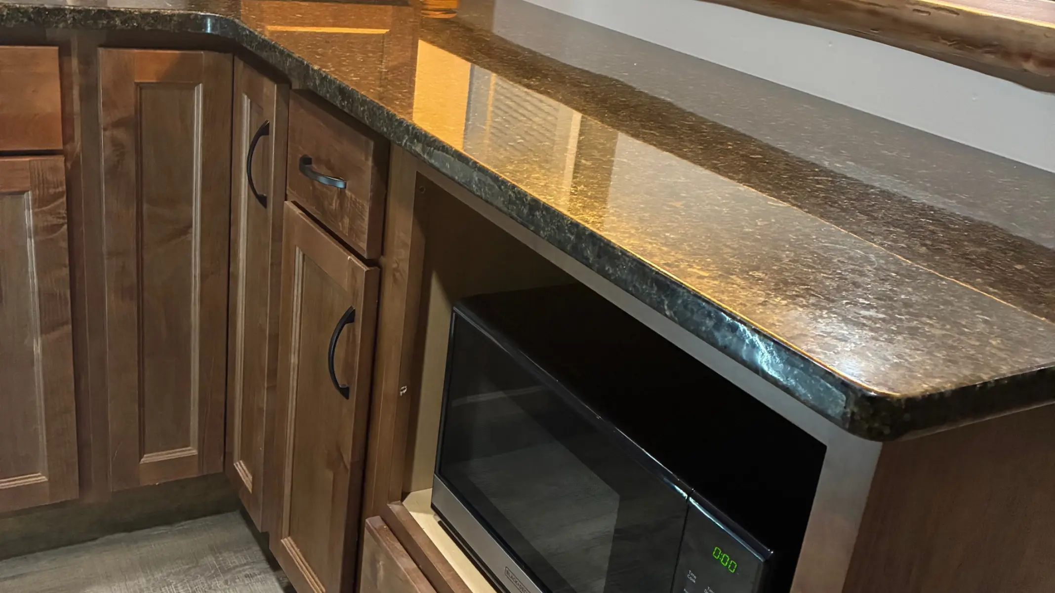 A kitchen corner with wooden cabinets, a dark granite countertop, and a built in microwave oven situated below the counter.